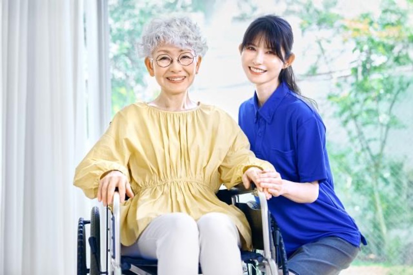 車椅子に座り笑顔の白髪女性と青色の制服を着た笑顔の女性ホームヘルパー 