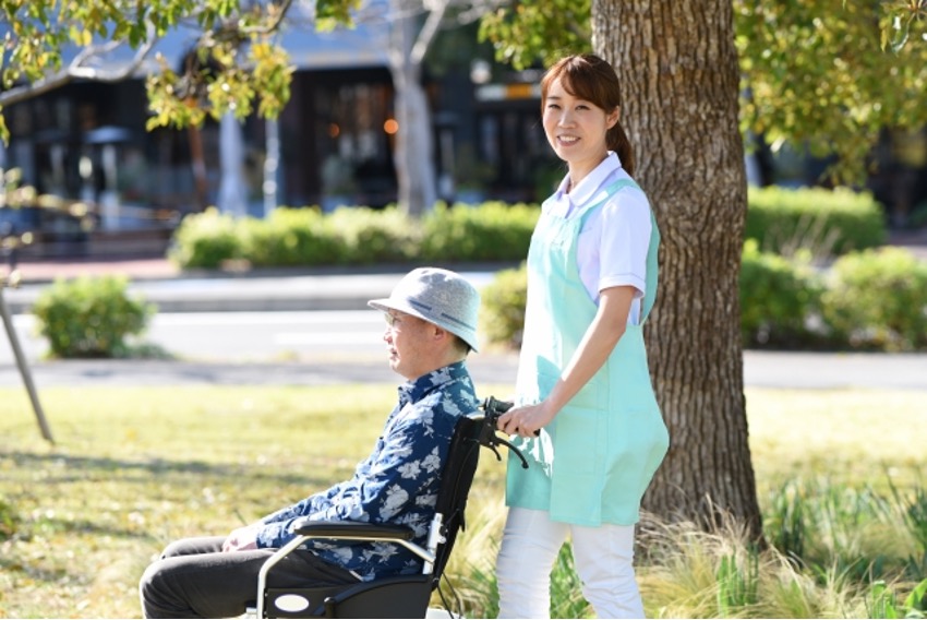 笑顔の女性介護スタッフが男性の乗る車いすを押している