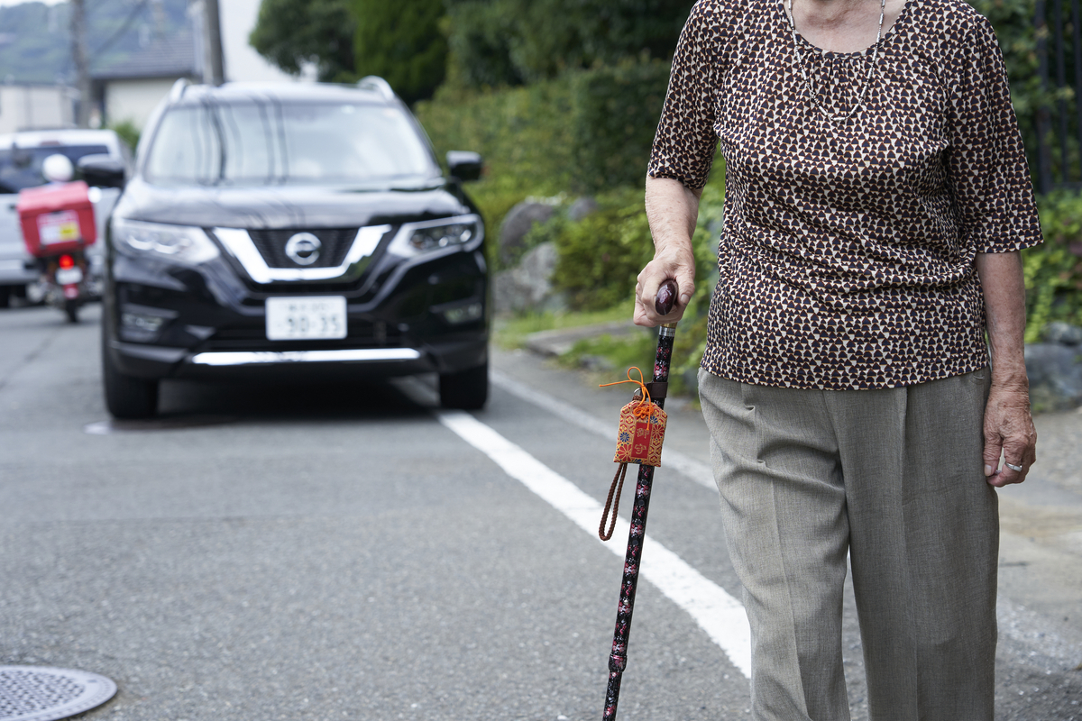 認知症徘徊GPSセンター御守りケースを杖につけて歩く女性