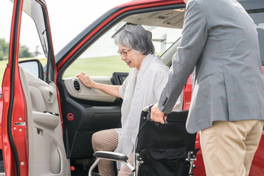 車から車椅子へ乗り移ろうとしている高齢女性と介護者