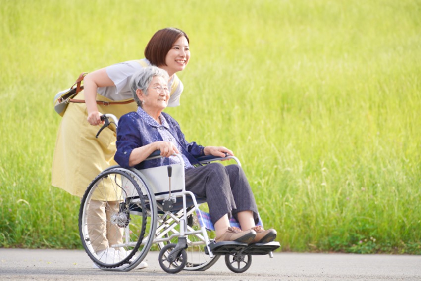 屋外で車椅子を押すヘルパーと笑顔の高齢者