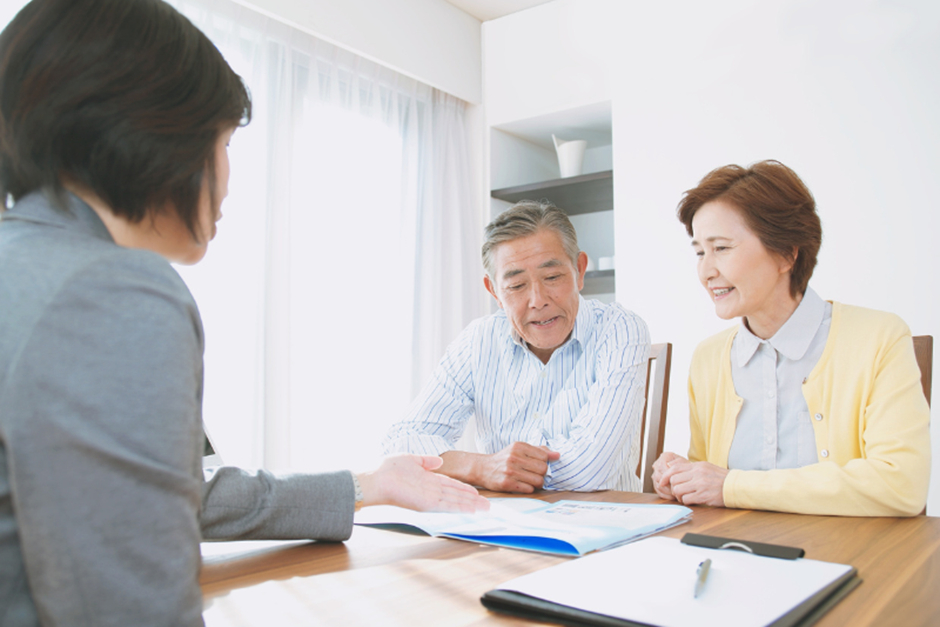 地域包括支援センターの職員が、高齢夫婦に介護保険や生活に関する相談・説明を行っている様子。