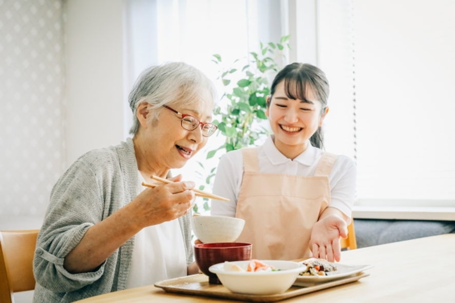 食事を提供する介護士と笑顔の高齢女性
