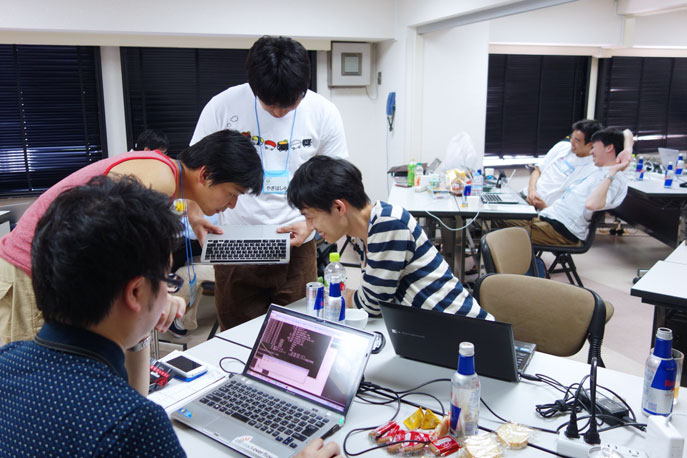 「バグハン」中のひとコマ。1人の参加者の端末を、他の参加者がのぞき込んでいる様子の写真。