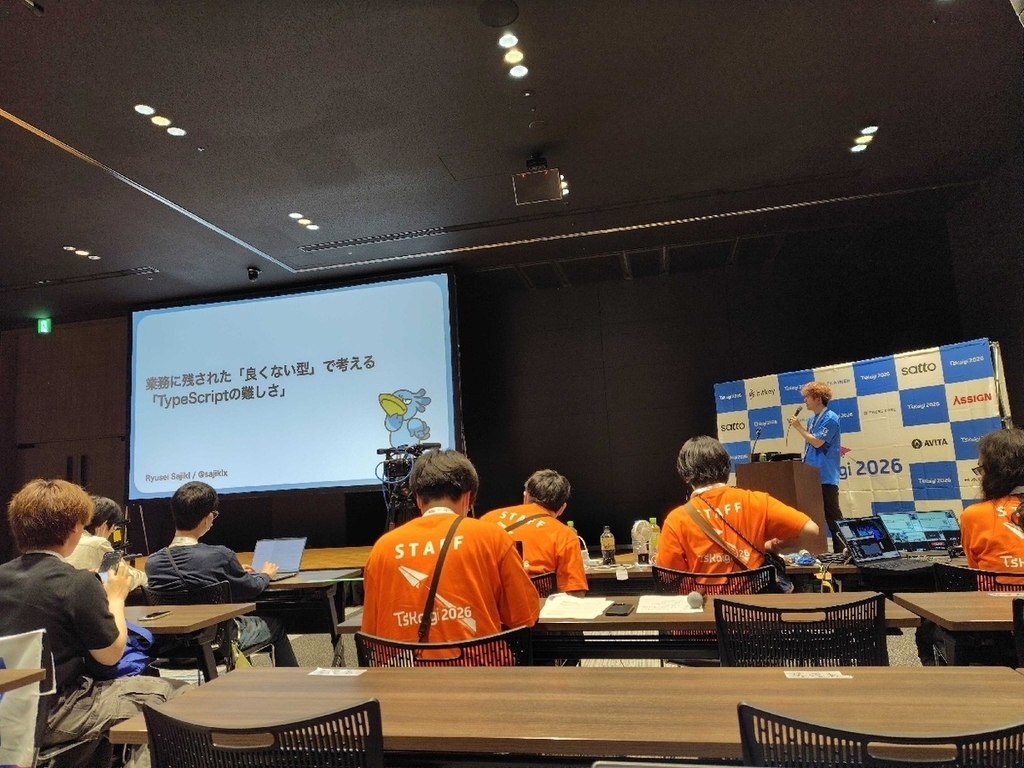 登壇中の法被を着ているSajiさん。スクリーンにはセッションのタイトルのスライドが映っている。