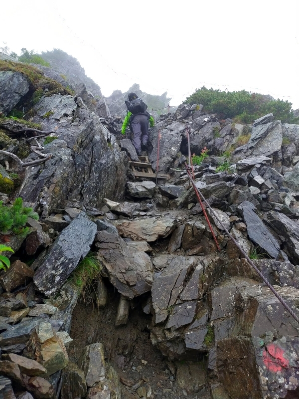 南アルプス北岳、雨に濡れた鎖場を登る登山者