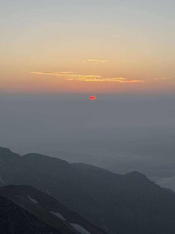雲の層に沈んでいく赤い夕日と、暗くなった稜線