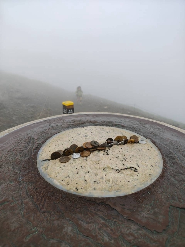 白馬岳山頂の方位盤に並べられた硬貨と、その先の白いガス
