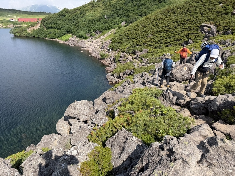 白馬大池の岸を通る大岩の道を歩く登山者たち