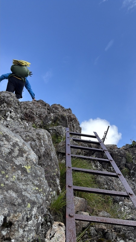 真教寺尾根の鉄梯子と、その上の岩を越えていく登山者