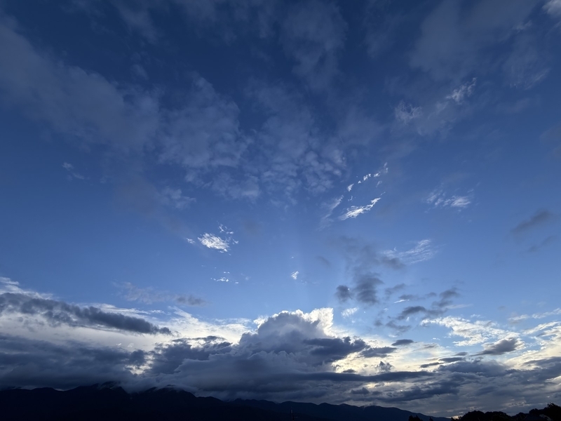 下山後の夕方の空。雲の切れ間から光芒が伸び、遠くの山並みがシルエットになっている