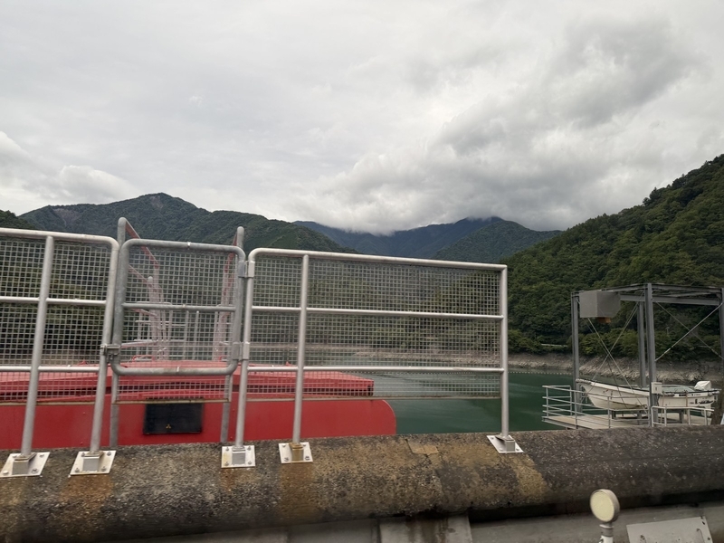 送迎バスの車窓から見た畑薙湖の緑の水面と、曇り空の山並み