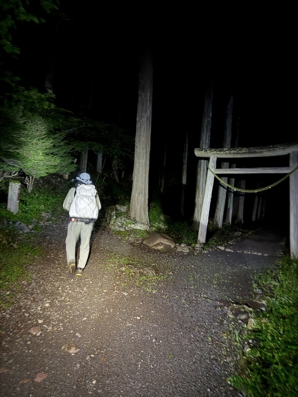 暗闇の中、ヘッドランプに照らされた鳥居と登山者