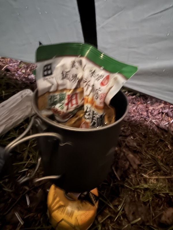 テントの中で、クッカーに入れて湯煎する田所商店監修の担々まぜ麺の袋