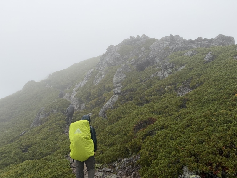 ガスに包まれた稜線を、黄色いザックカバーの登山者が登っていく
