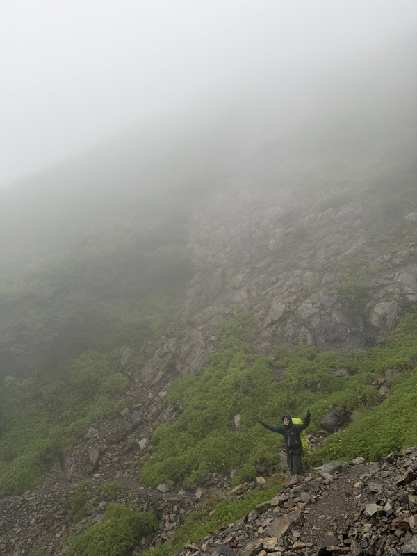 ガスの斜面を、両手を広げた登山者が下っていく