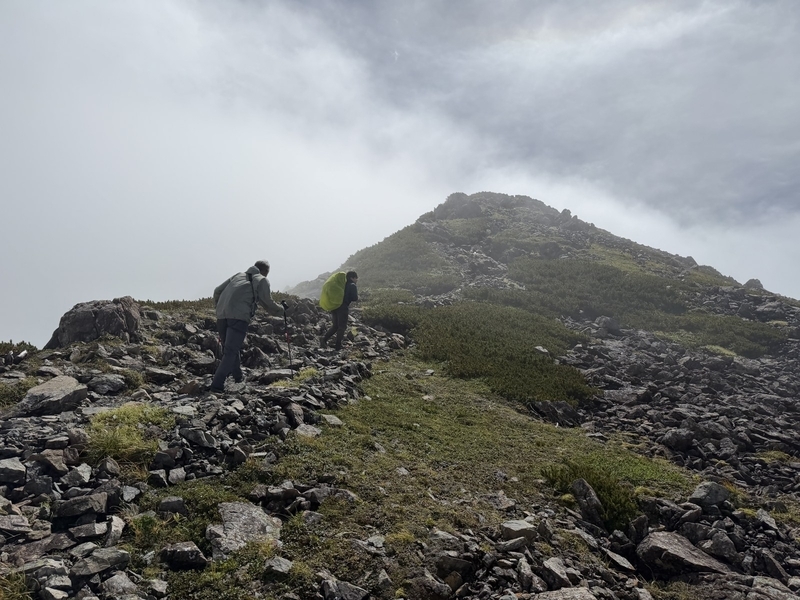 雲が抜けていく赤石岳へ、稜線を登っていく登山者たち