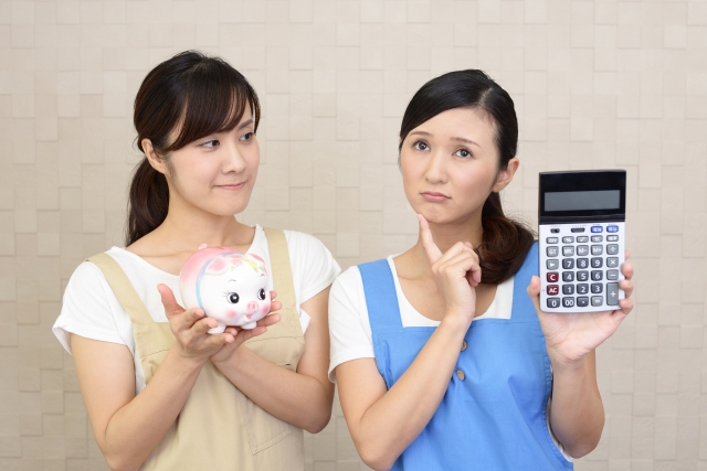 豚の貯金箱と計算機を持つ二人の女性の画像