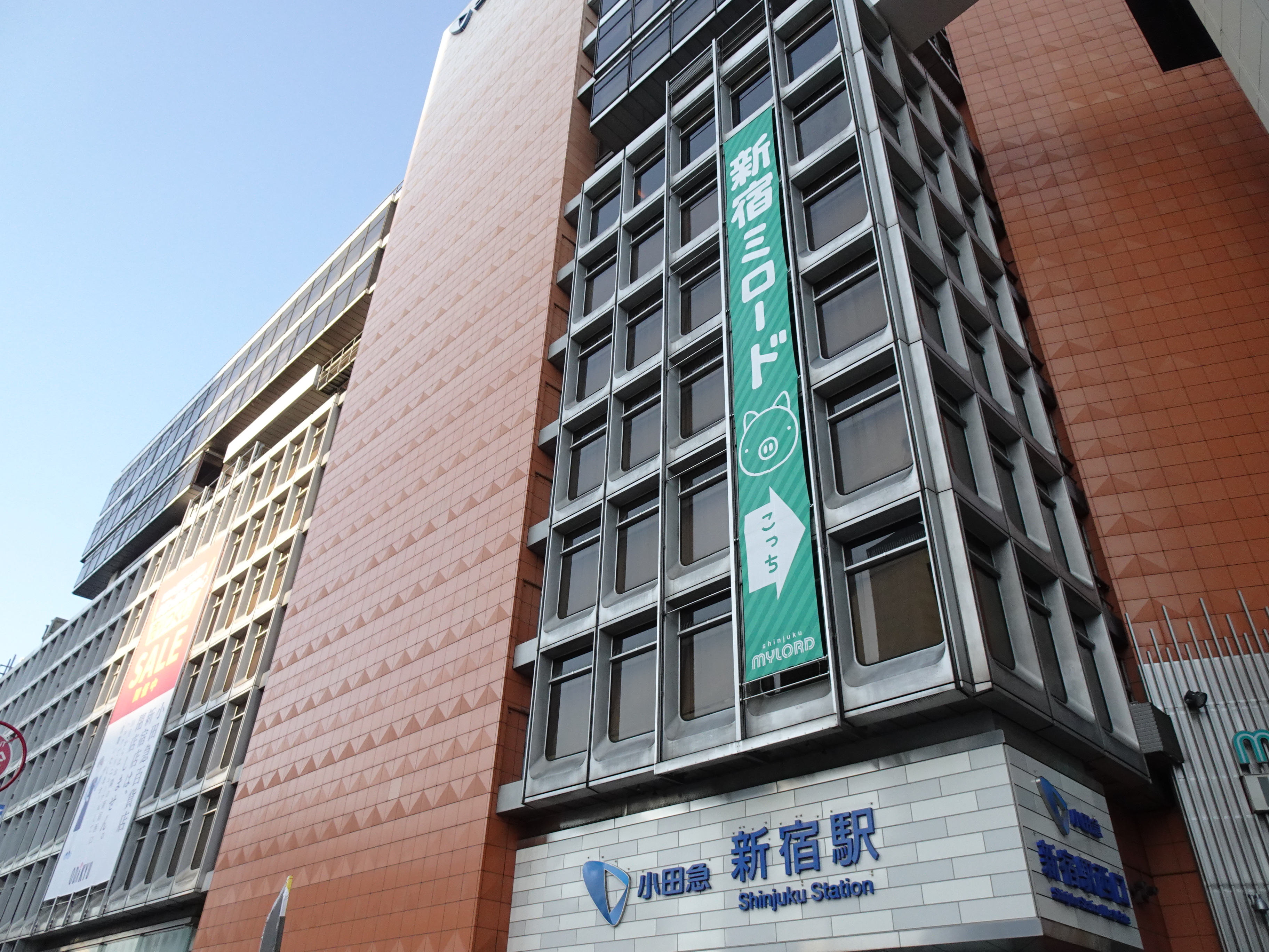 新宿ミロードの方向を示す緑色の垂れ幕には「こっち」という右方向の矢印と可愛らしくほのぼのとした雰囲気のブタの顔の絵が描かれている