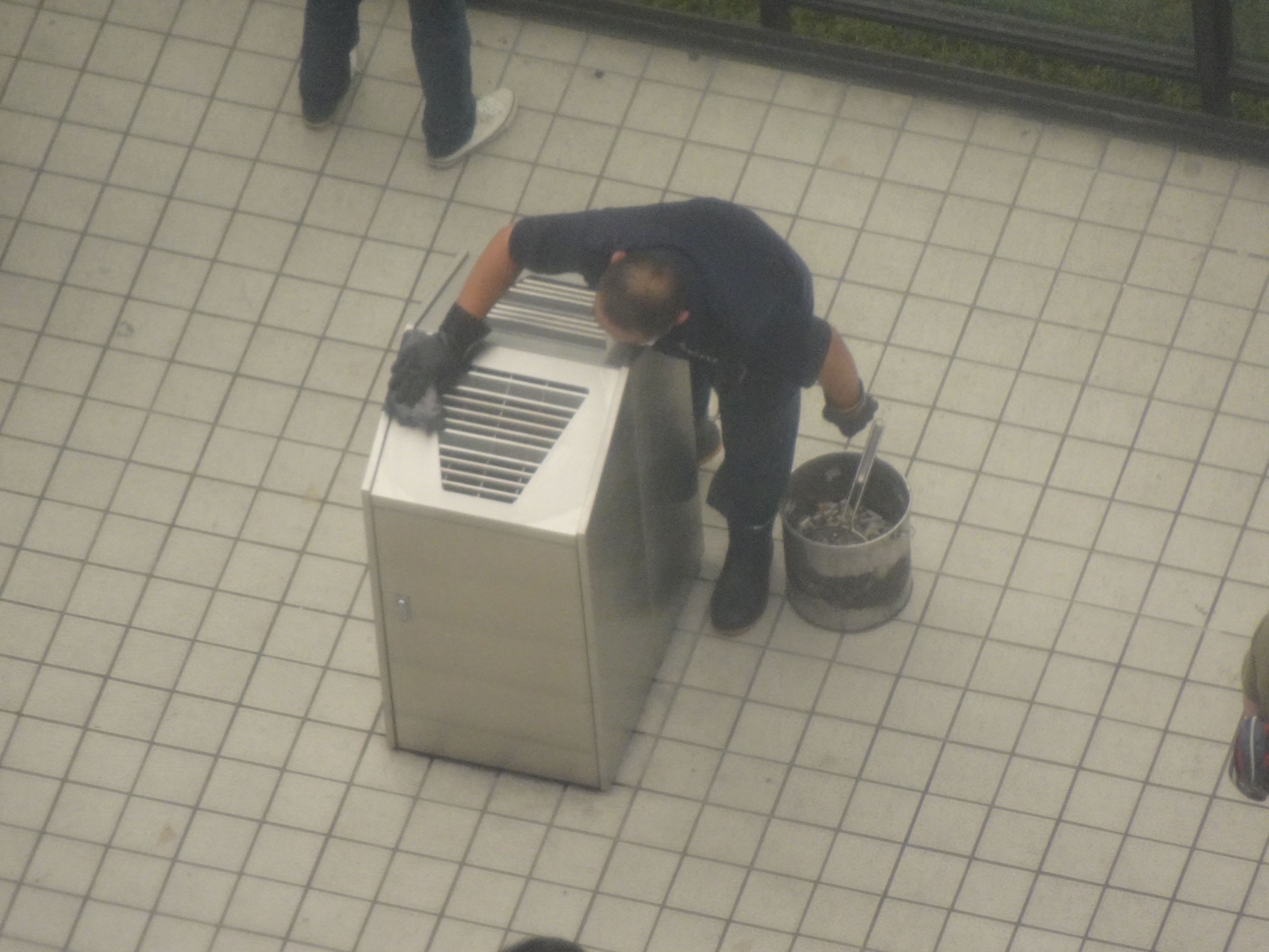 新宿駅西口喫煙所の吸い殻入れを清掃する人の姿