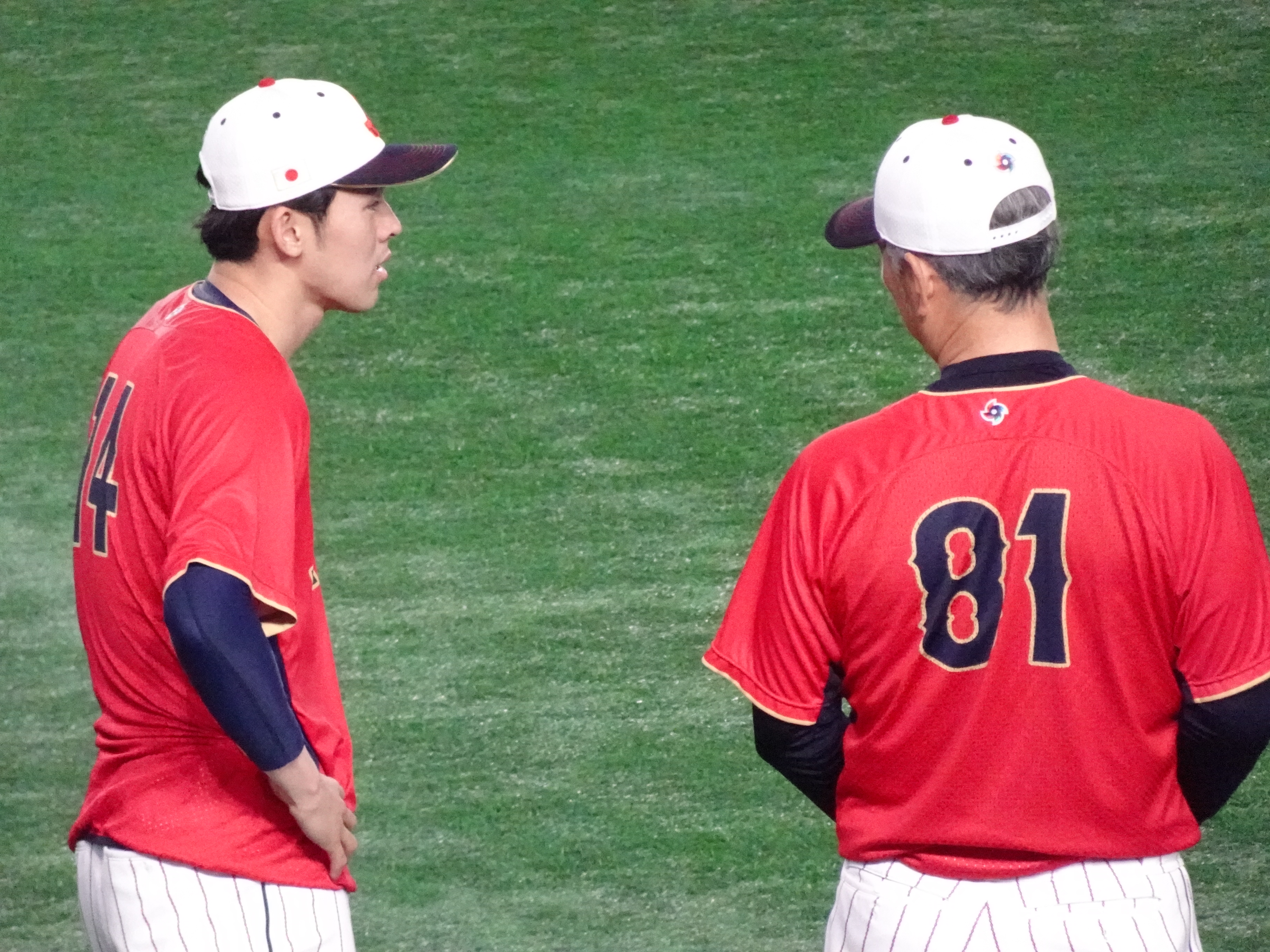 日本対イタリア戦の試合前、外野でウォーミングアップをする佐々木朗希投手(左)と話をする吉井理人投手コーチ(右)の姿。
