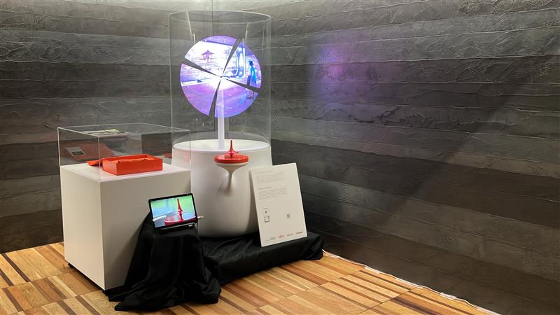 川崎市役所の本庁舎展望フロアに展示した際のブースの画像。黒い壁紙と木目調の床で出来た展望フロアの隅に展示フロアが設けられている。ワンダリングアーカイブスの筐体に加えて、本取り組みの説明パネルやアンケート回答用のタブレットも配置されている。
