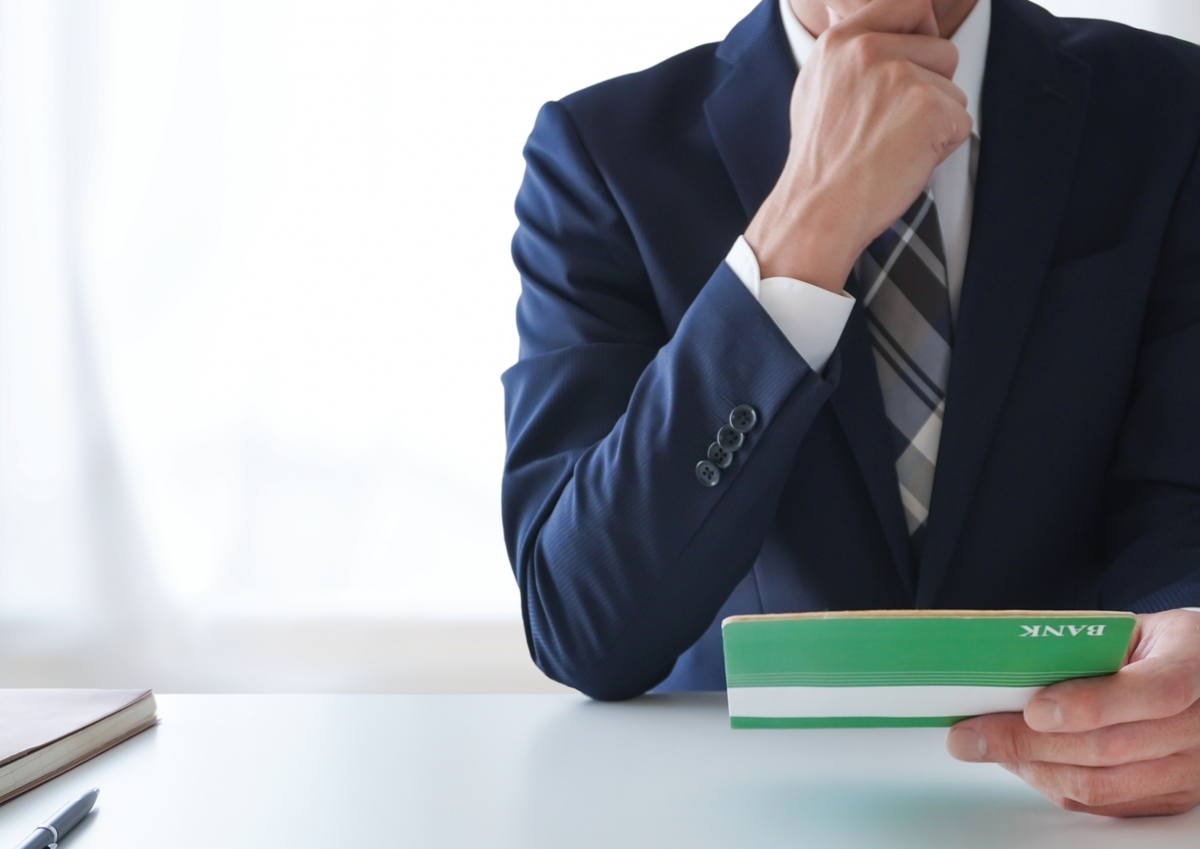 通帳を眺めるスーツの男性