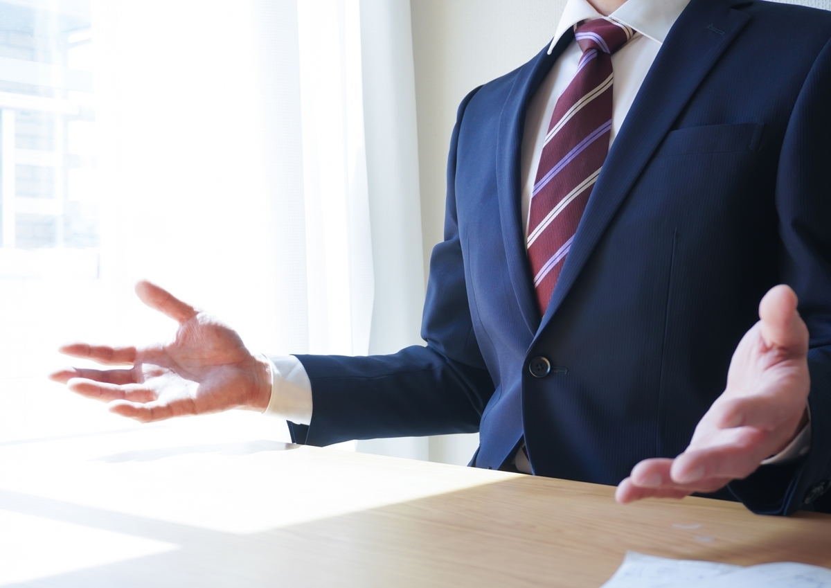 両手を広げ話しをしているスーツの男性