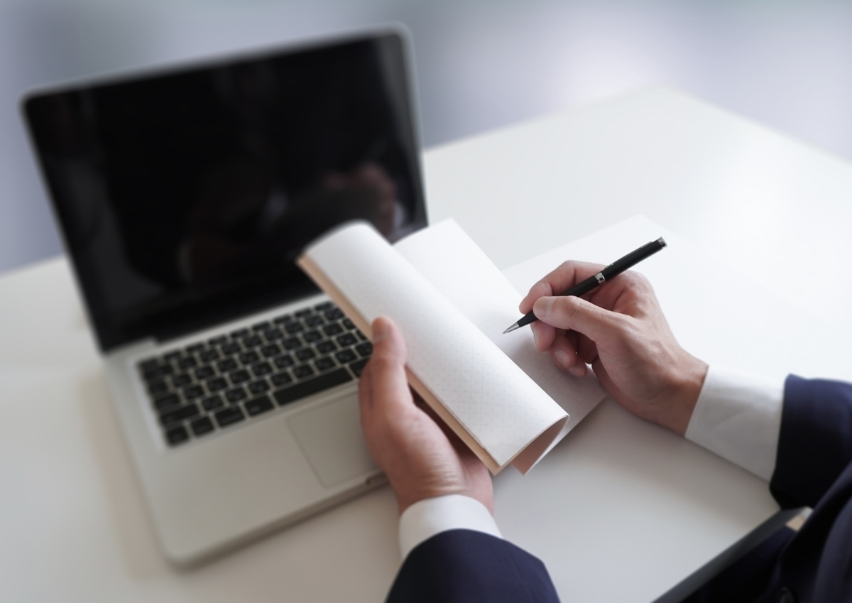 デスクで手帳に書き込むスーツの男性