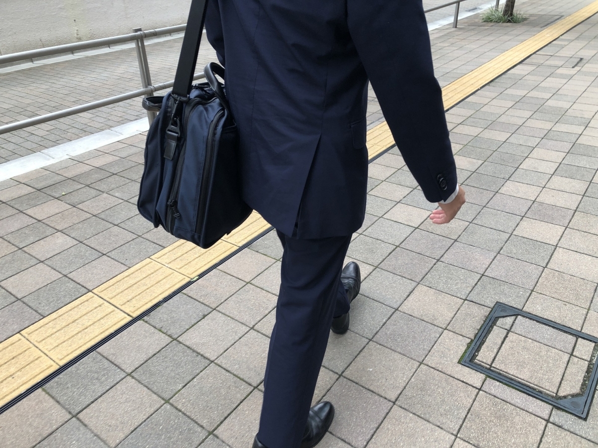 肩にカバンをかけ歩くスーツ姿の男性