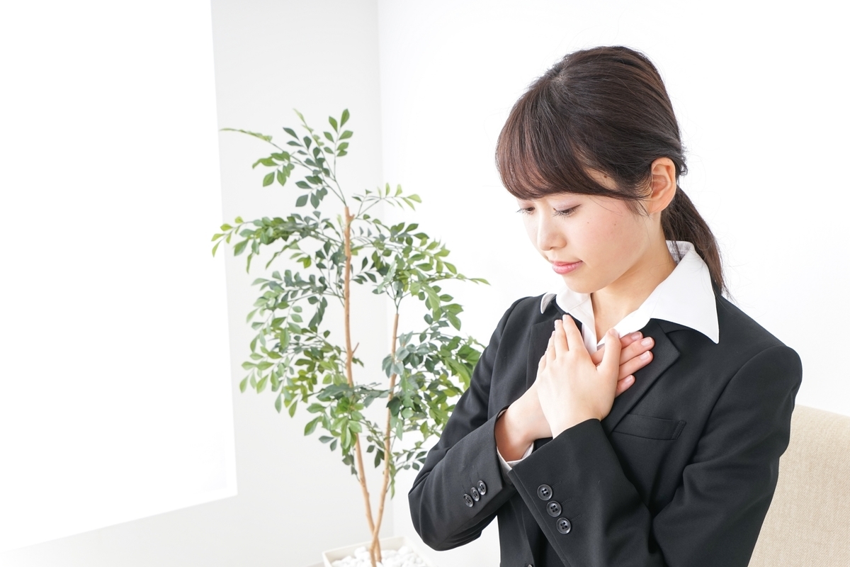 胸に手を当て目をつむるスーツ姿の女性