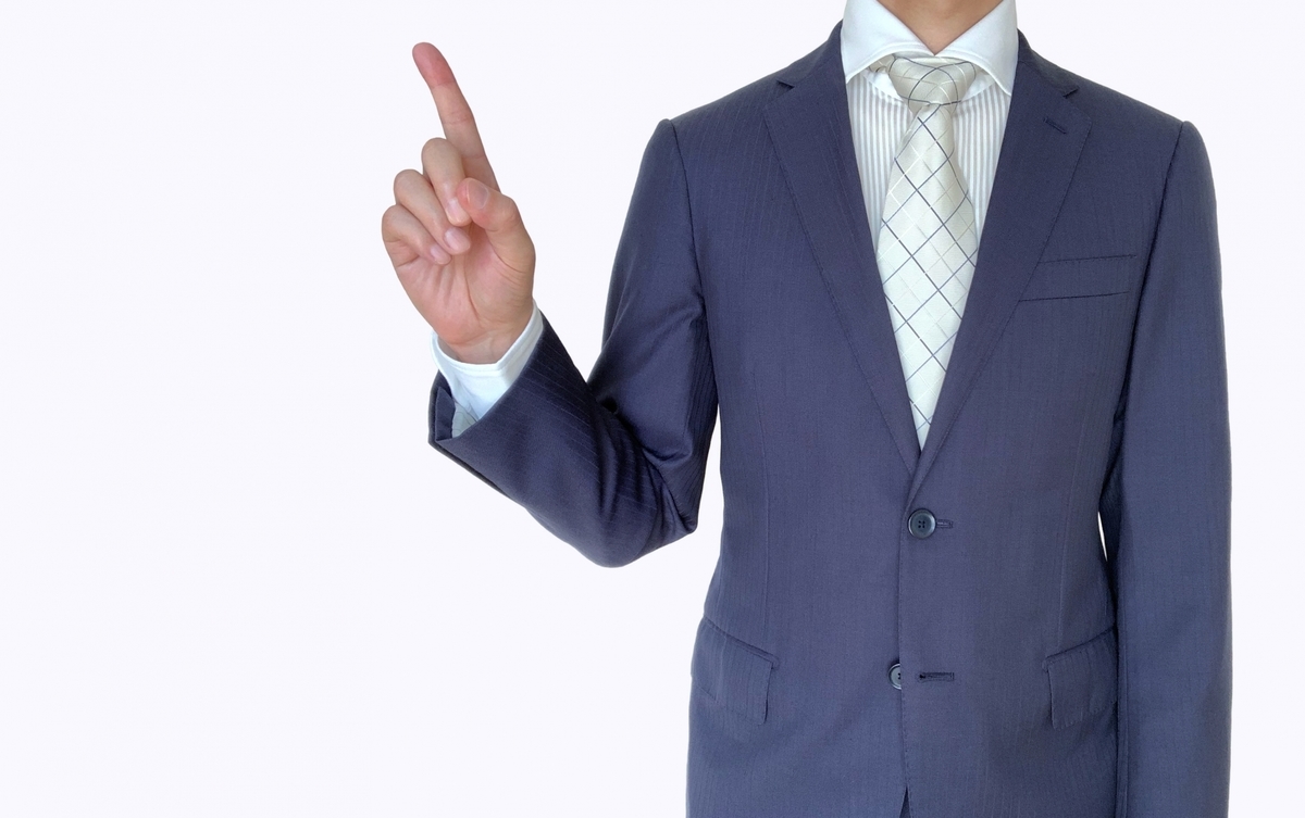 人差し指を上に向けるスーツ姿の男性