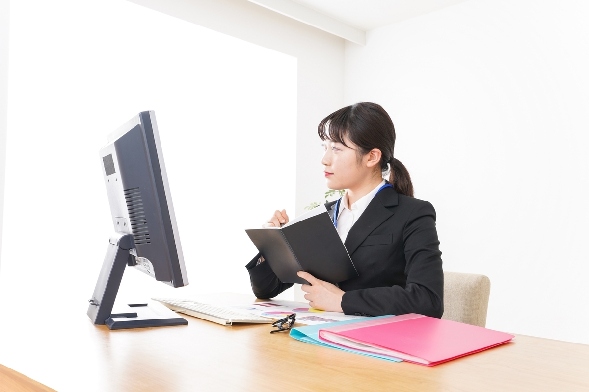 パソコンを見ながら手帳に記入する