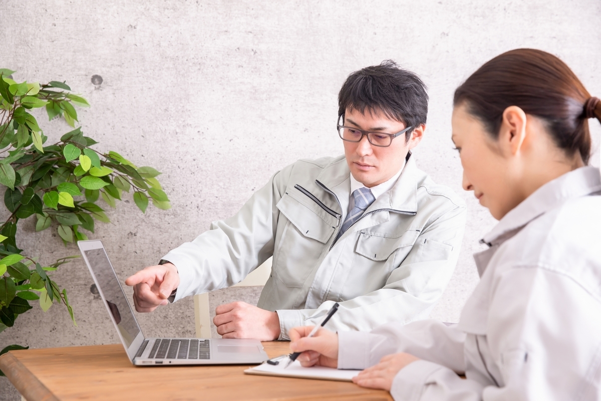 パソコンを見ながら話す作業着の2人