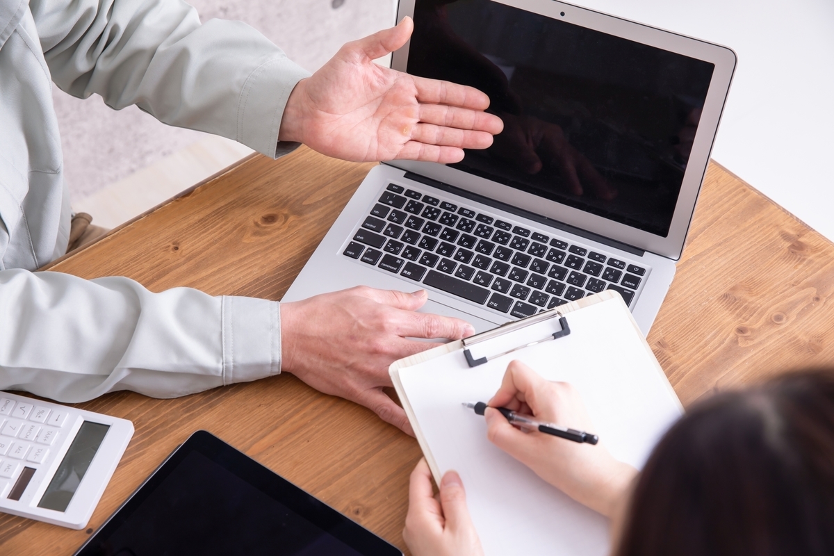 パソコンを挟み打ち合わせをする作業着の男性