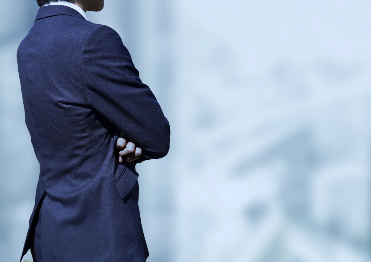 腕組みをするスーツの男性の後姿