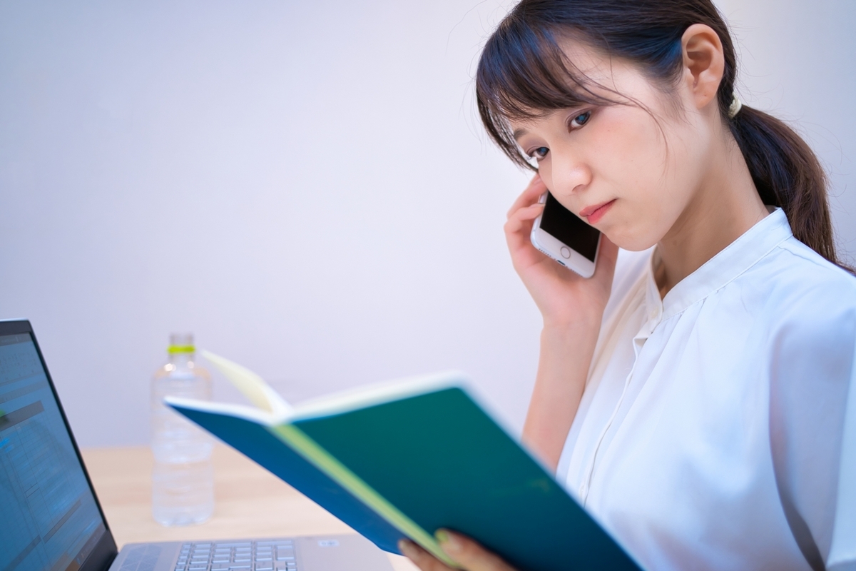 手帳を見ながら電話する女性