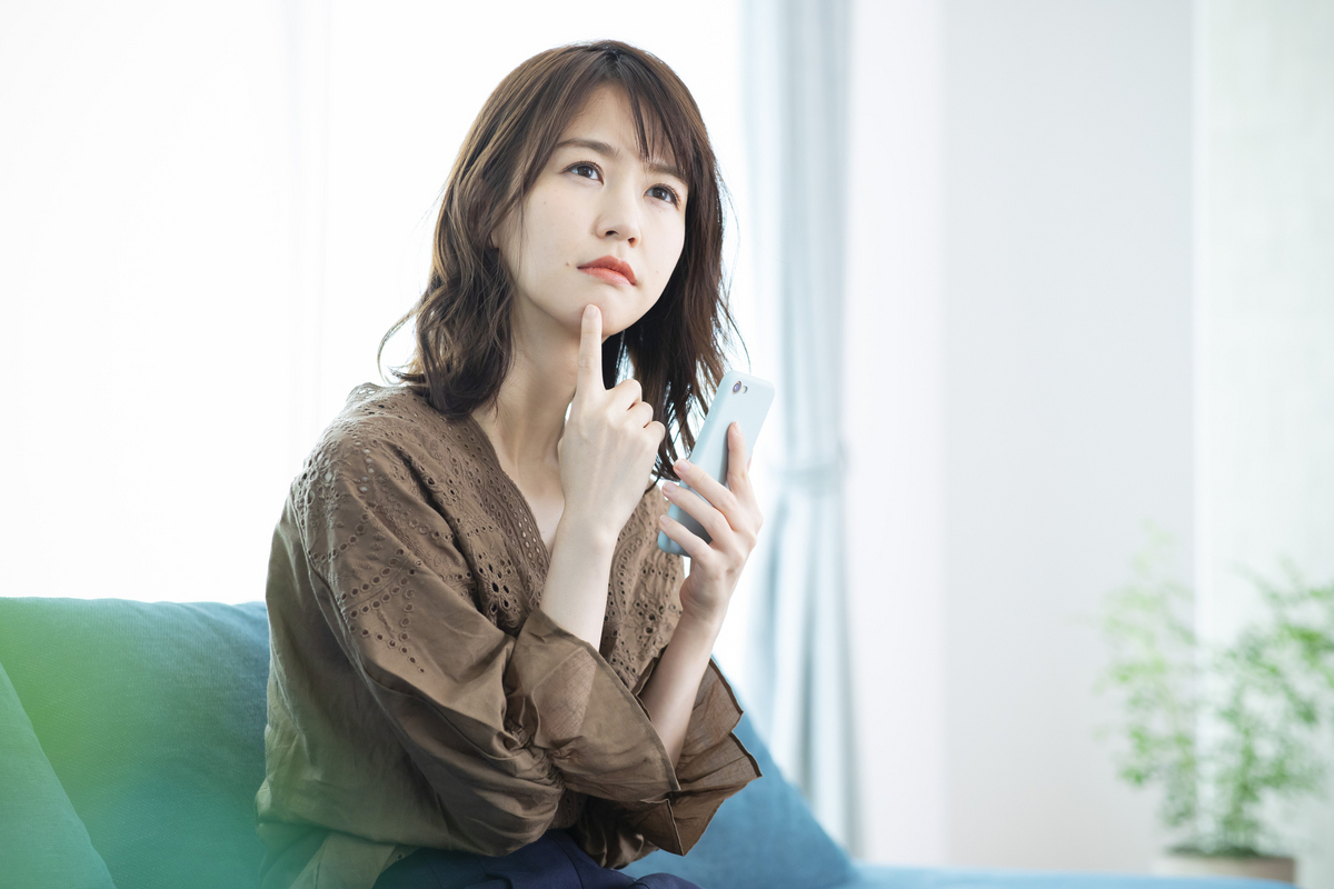 スマホを手に考える女性