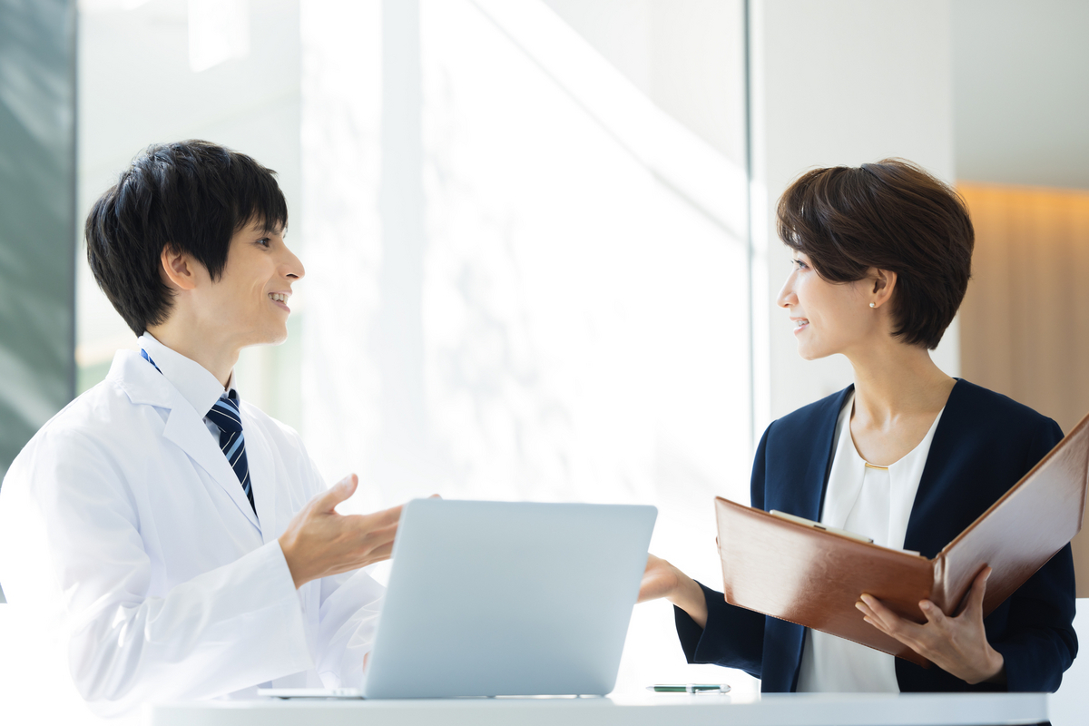 打ち合わせをする白衣の人物とビジネスパーソン