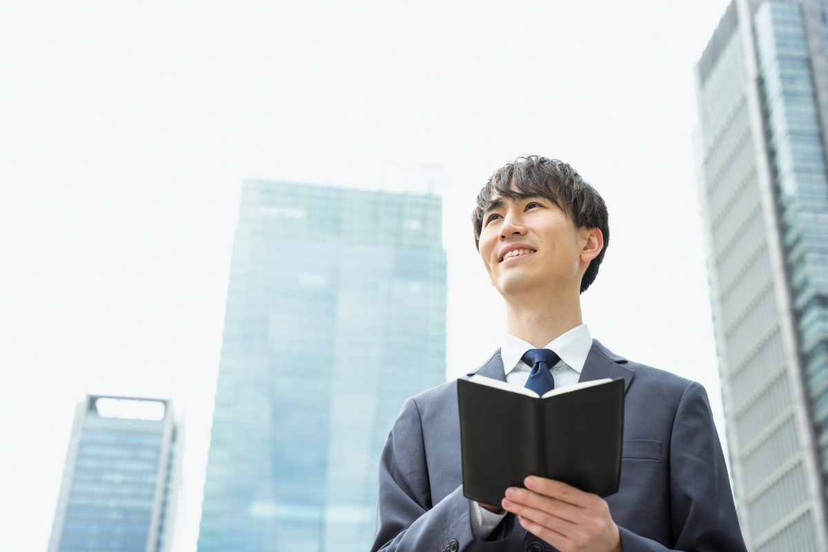 手帳を手に空を見るビジネスパーソン