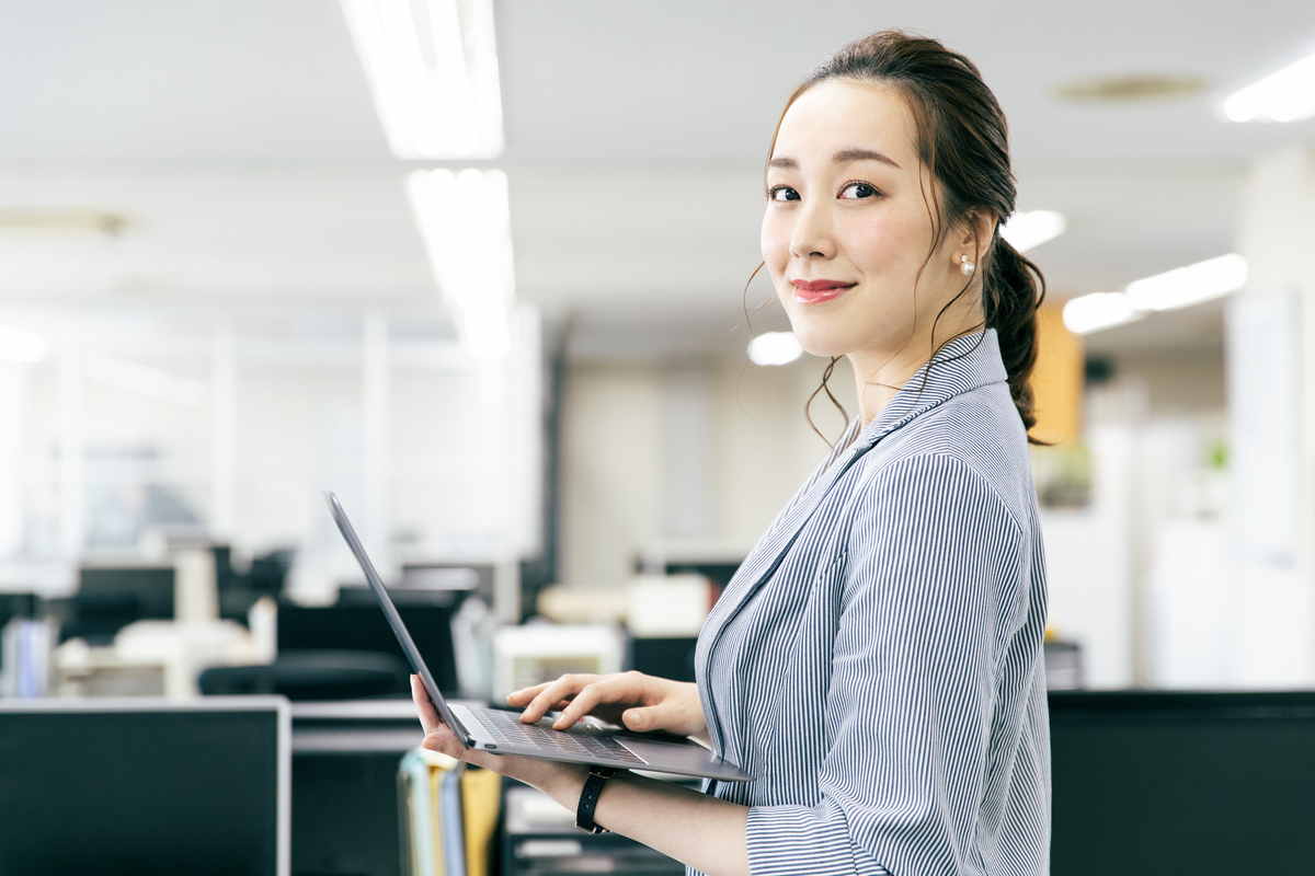 ノートパソコンを持ってオフィスで立つ人物