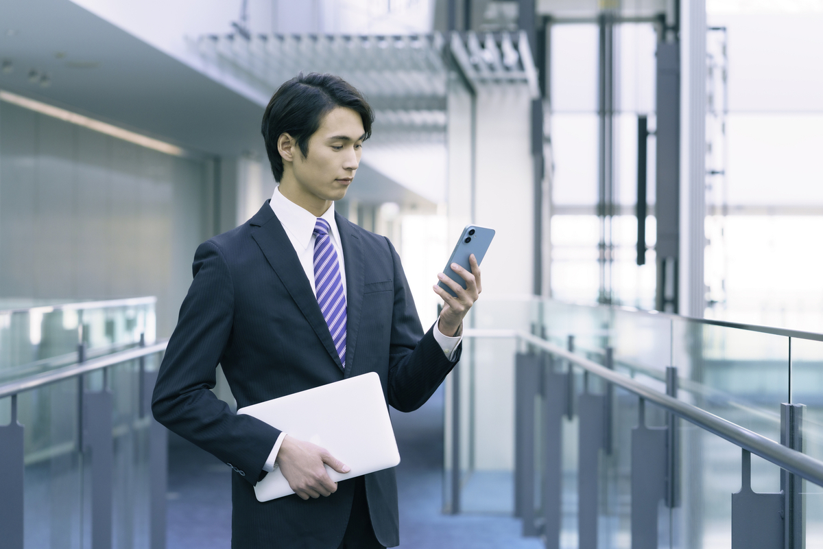 ノートパソコンを小脇に抱えスマホを見る男性