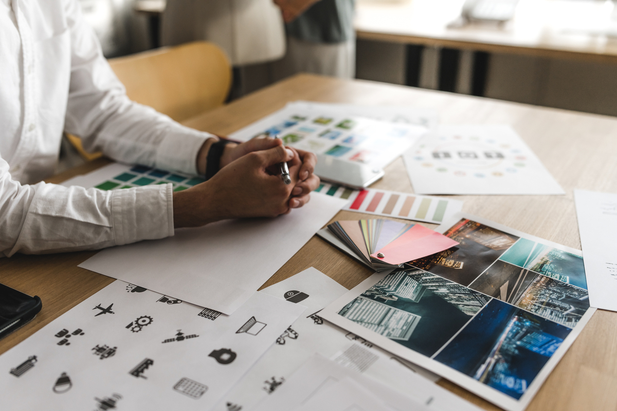 机に広がるデザイナー用資料と男性の手元