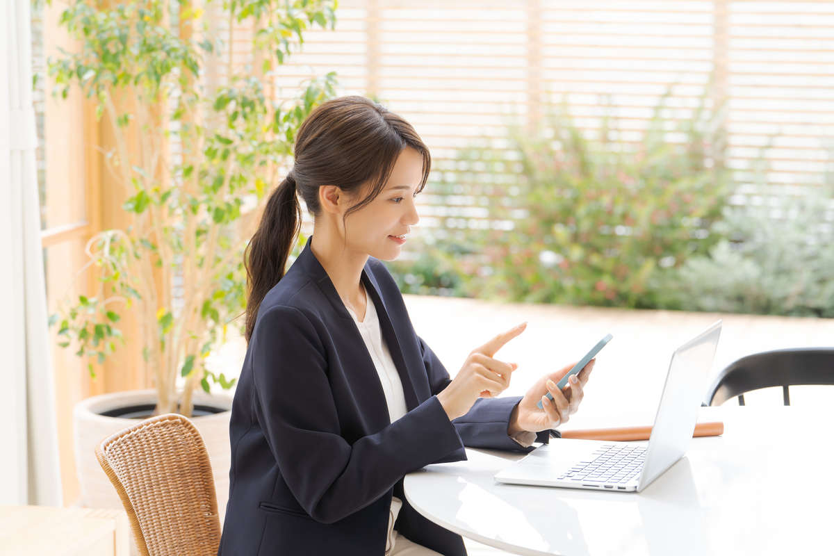 パソコンの前でスマホ操作をする女性