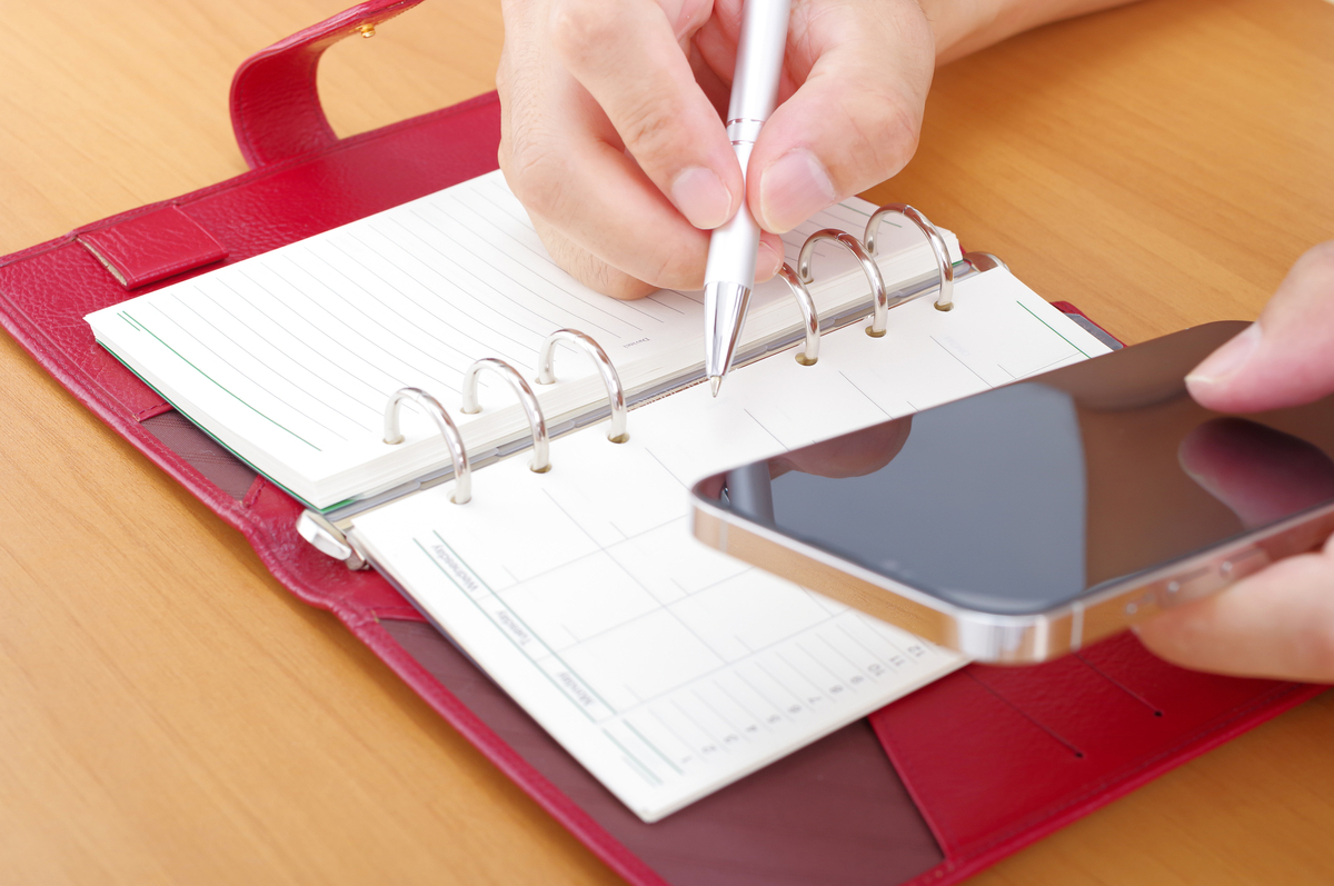 スマホを見ながら手帳を書き込む人の手元
