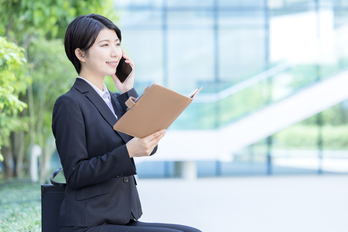 外でファイルを開き電話をする女性
