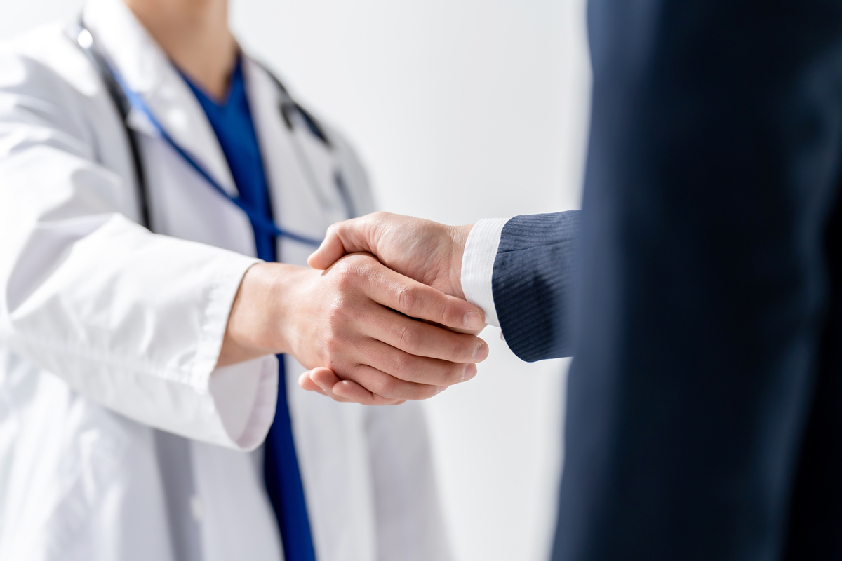 握手をするスーツの男性と医療従事者の手元