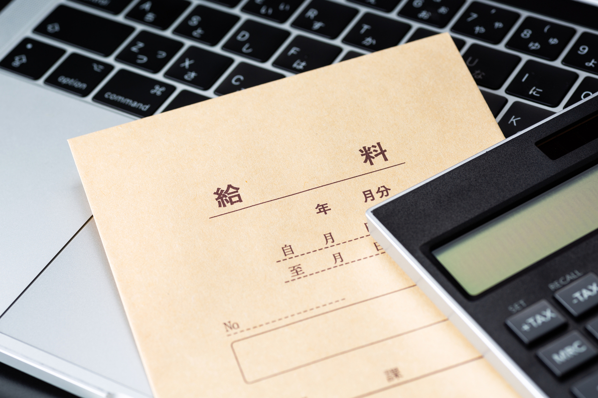 ノートパソコンの上に置かれた給料袋と電卓