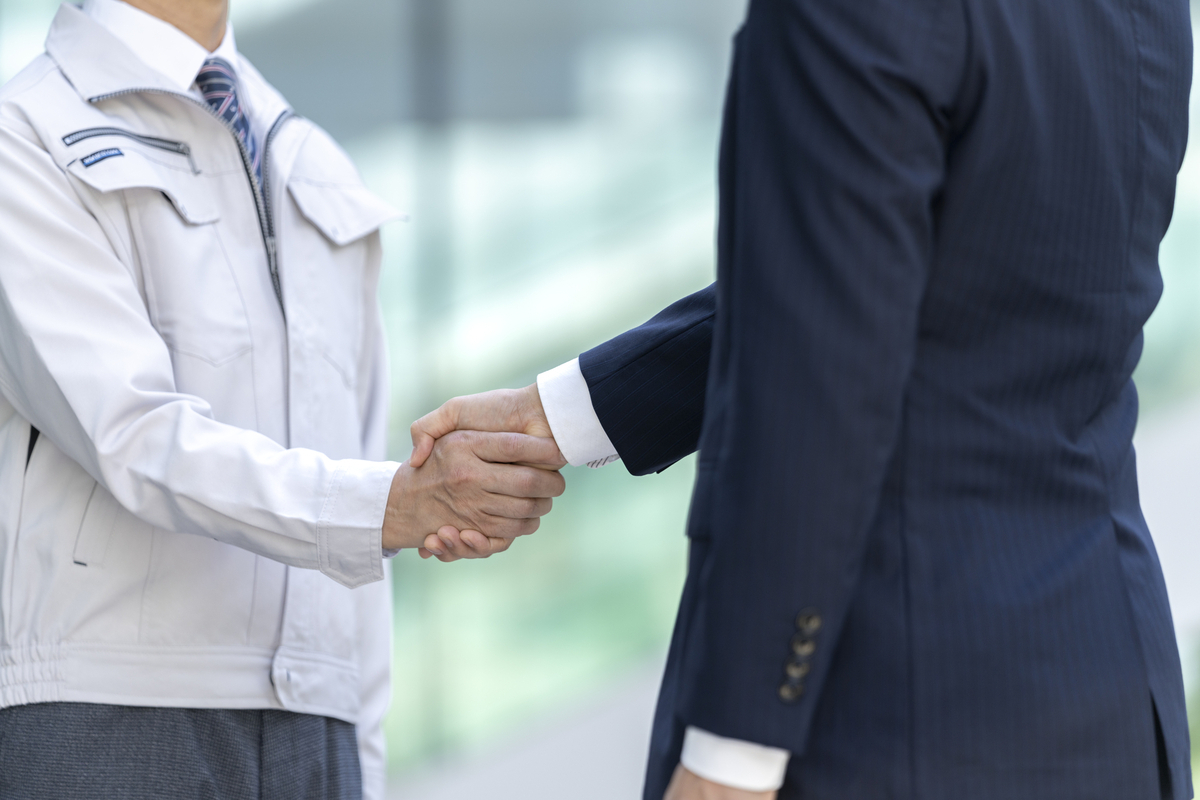 握手する作業服とスーツの男性