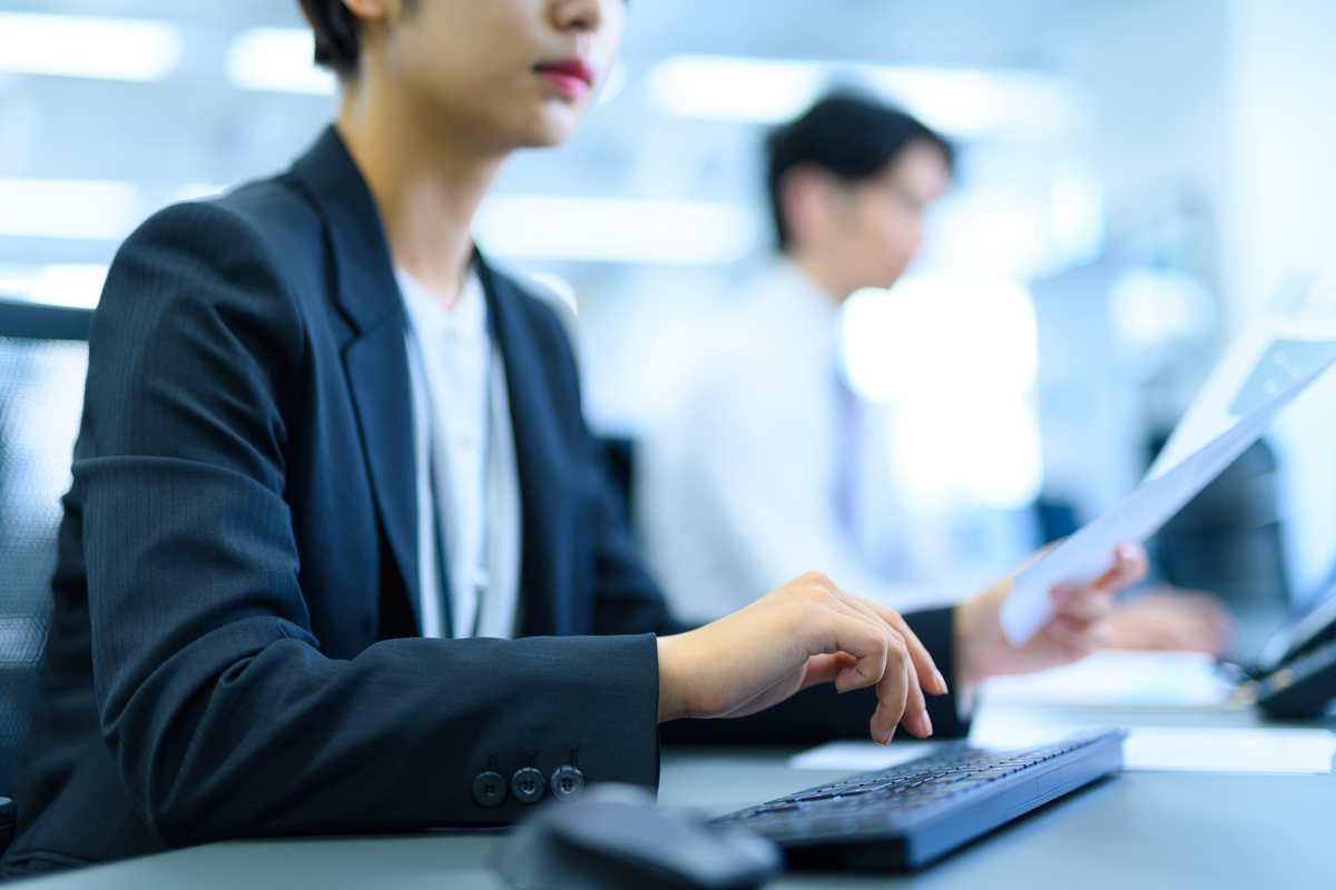 書類を片手にキーボードを打つ女性の手元